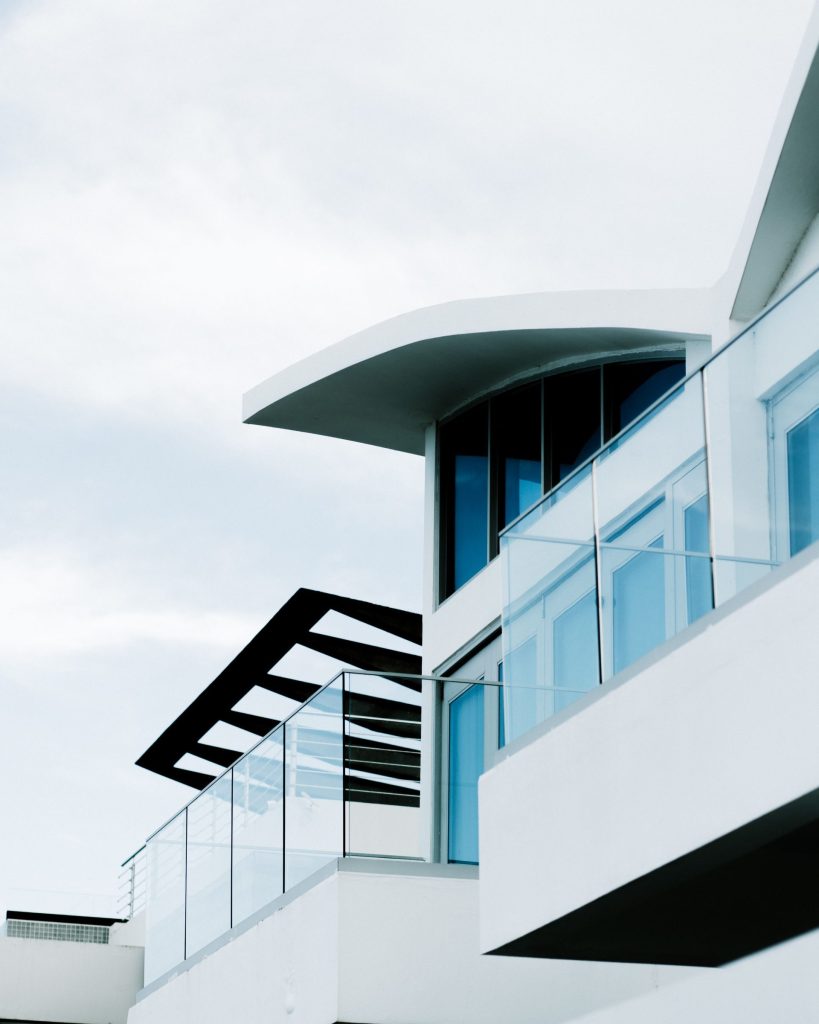 Low angle view of a modern building featuring glass balconies against a cloudy sky.